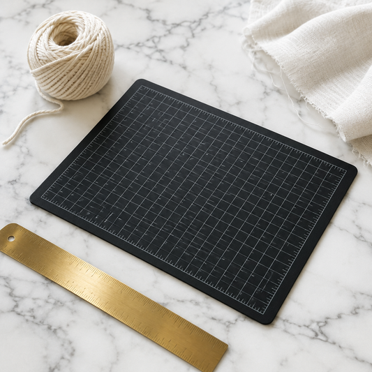 Planche de découpe noire quadrillée 30x22 cm sur un plan en marbre blanc avec règle en laiton et lin écru