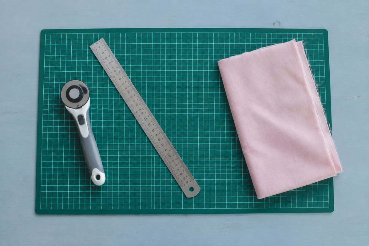 Planche de découpe verte quadrillée 45x30 cm sur une table bleu gris avec cutter rotatif, règle et tissu rose